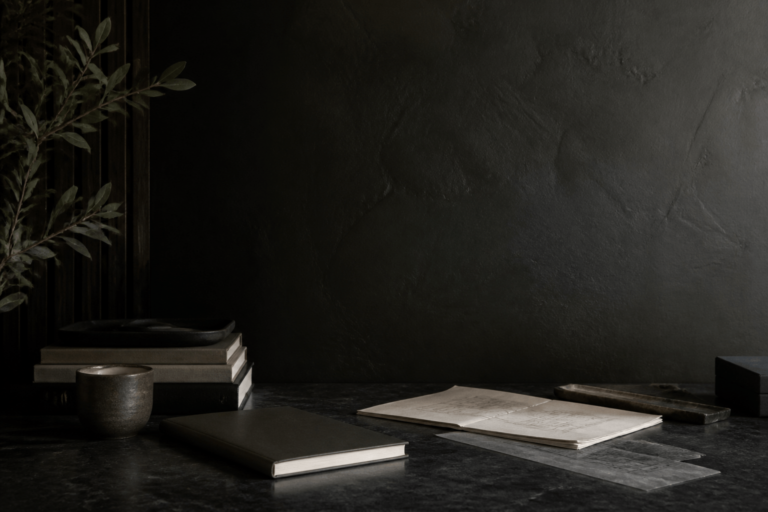 Dunkler Studio-Arbeitsplatz mit Steinoberfläche, Notizbuch, Büchern und architektonischer Textur.